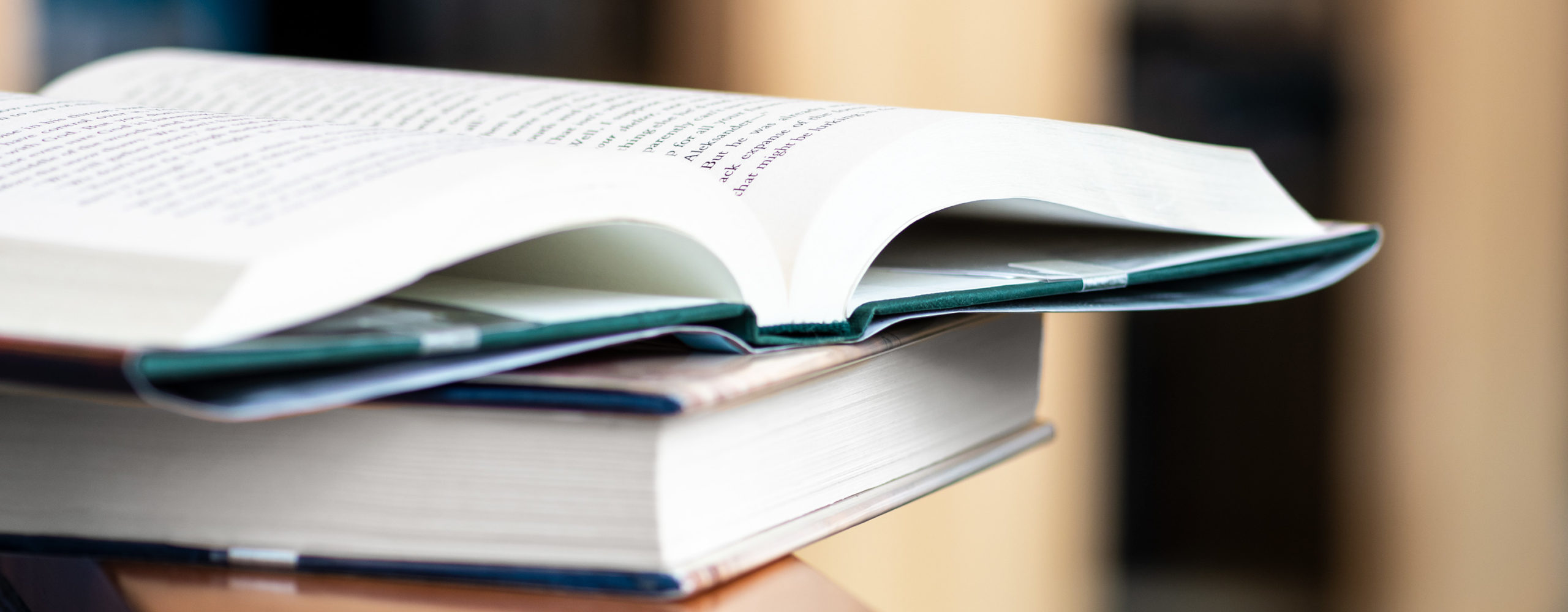 Open book resting on another book on a countertop, with a softly blurred background.